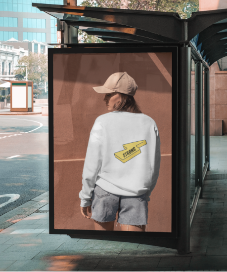 Person wearing a white sweatshirt with a yellow logo in front of a TISART branded bus stop.