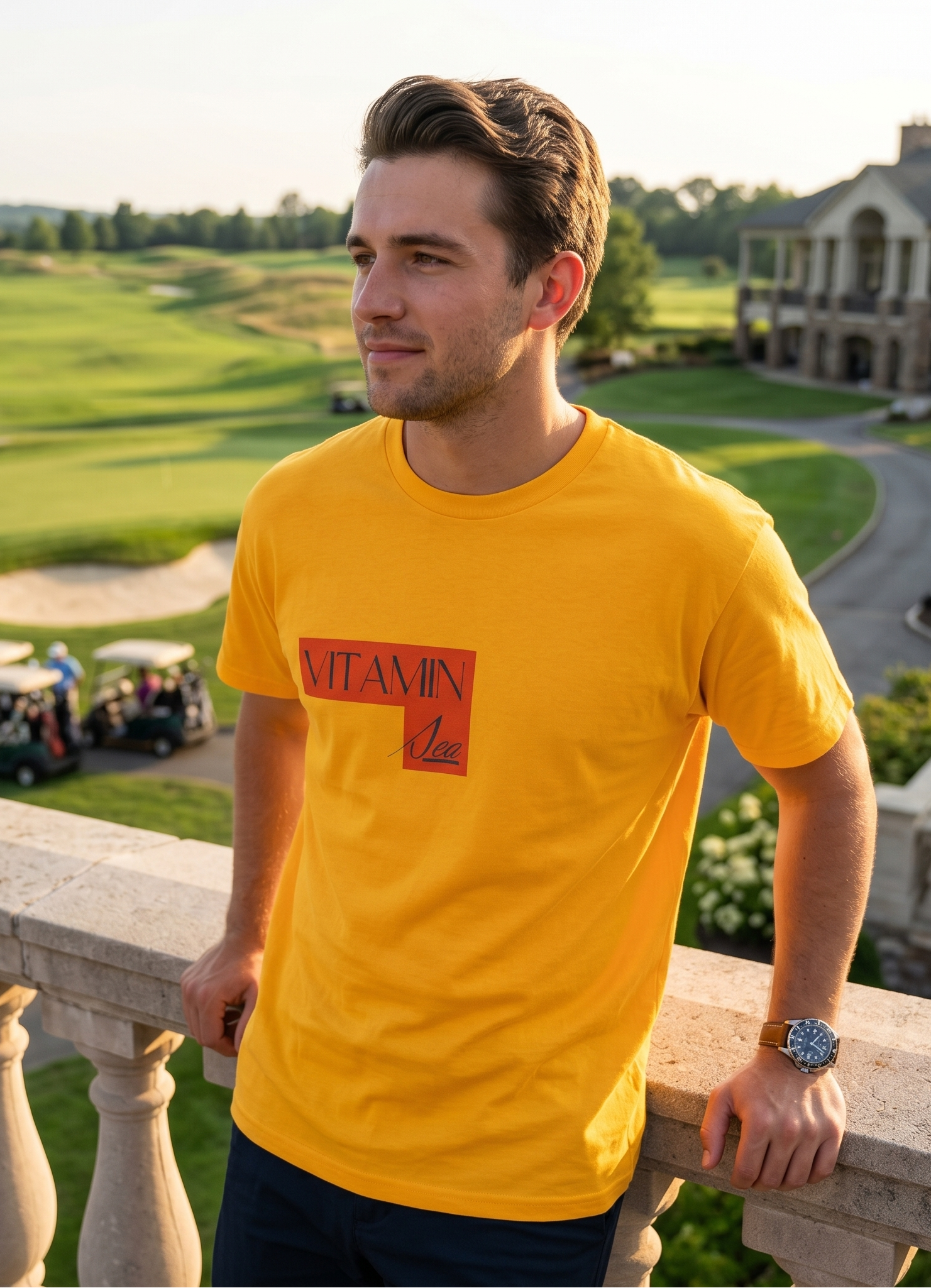 Man wearing a yellow t-shirt with a logo, standing on a balcony overlooking a golf course.